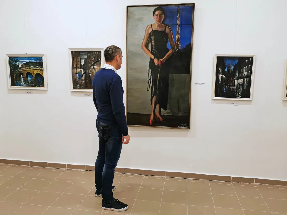 Életnagyságú önarckép. A művésznő fekete ruhában, piros cipőben, kezében piros virágot tart, jobb szemén monokli., Corini Margit festőművész születésének 125., halálának 40. évfordulójára rendezett emlékkiállítás, Vidovszky Béla Városi Képtár, Gyomaendrőd