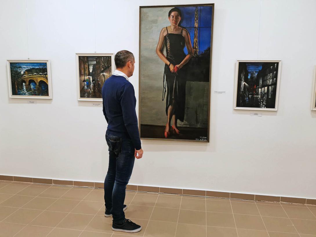 Életnagyságú önarckép. A művésznő fekete ruhában, piros cipőben, kezében piros virágot tart, jobb szemén monokli., Corini Margit festőművész születésének 125., halálának 40. évfordulójára rendezett emlékkiállítás, Vidovszky Béla Városi Képtár, Gyomaendrőd
